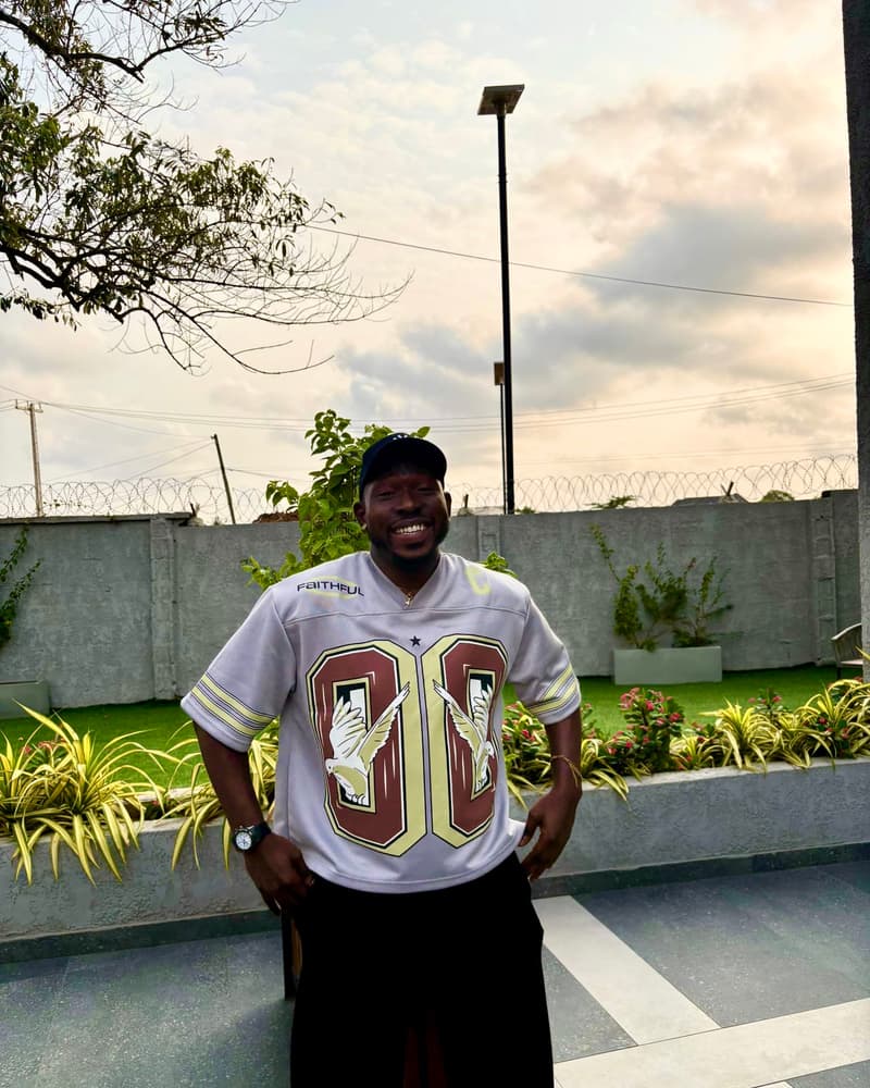 A man in a cap and a white American football jersey smiling in a landscaped garden at dusk